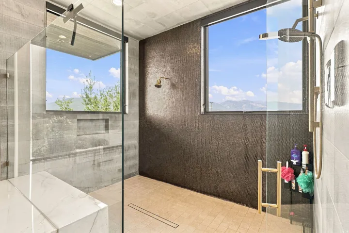 Glass-enclosed shower featuring a built-in bench, two windows, textured accent wall, and a linear drain