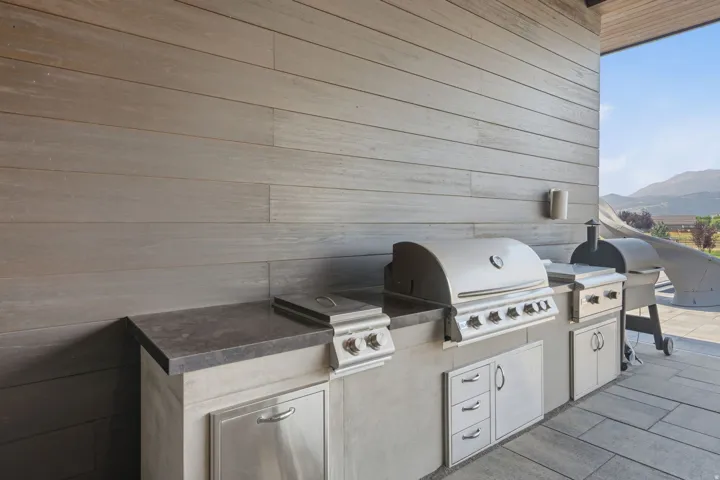 Outdoor kitchen featuring a built-in stainless steel grill, integrated cooktop, stainless steel cabinetry, stone countertops, and plank-style wall paneling