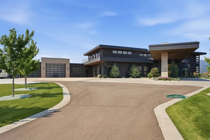 Modern exterior architecture with dark siding and stone accents, featuring a multi-car garage with glass panel doors, a paved driveway, and a covered entry