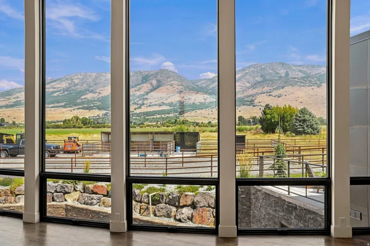 Floor-to-ceiling windows with black frames, showcasing mountainous terrain, expansive fields, and a rock garden