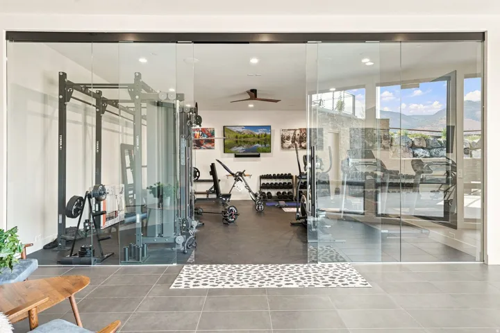 Glass panel sliding doors open to a dedicated fitness space featuring dark rubber flooring and a ceiling fan