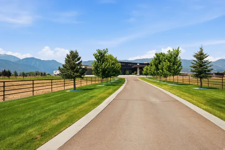 Paved drive with concrete border, manicured lawn, established trees, and mountain scenery
