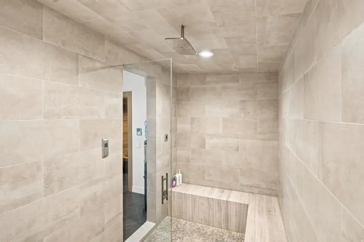 Spacious shower enclosure with floor-to-ceiling tile, a built-in bench, glass panel, and a rainfall showerhead