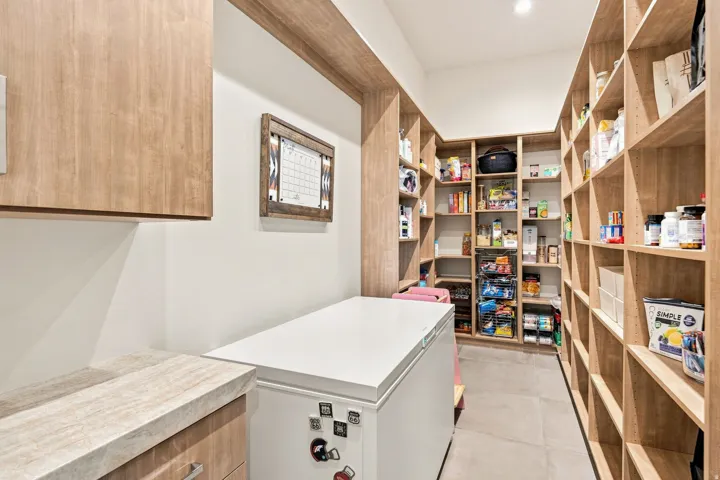 Expansive pantry featuring extensive wood-finish shelving, overhead recessed lighting, and durable tile flooring