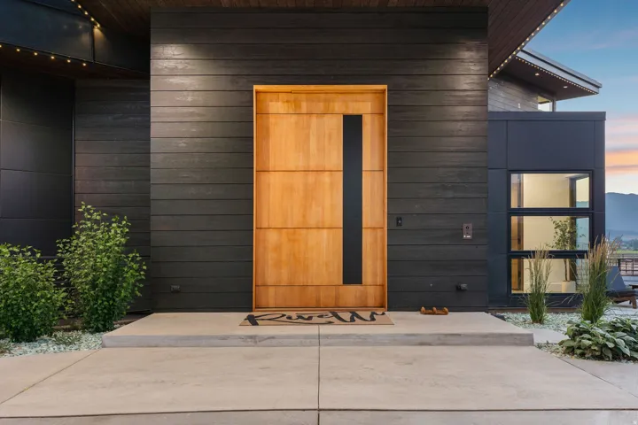 Modern exterior with dark horizontal siding, natural wood entry door, and multi-pane windows