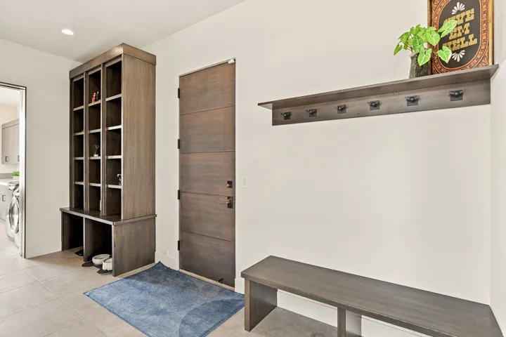 Built-in wood-finish shelving unit, wood-finish panel door, wood-finish wall-mounted shelf with hooks, and wood-finish bench