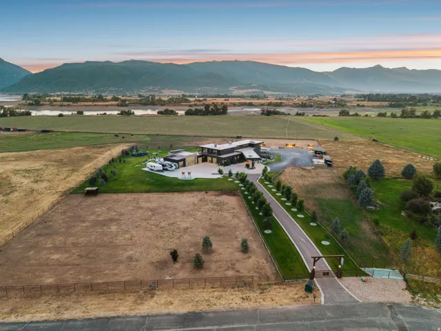 Expansive property featuring a paved entry drive, manicured lawns, mature trees, and mountainous scenery