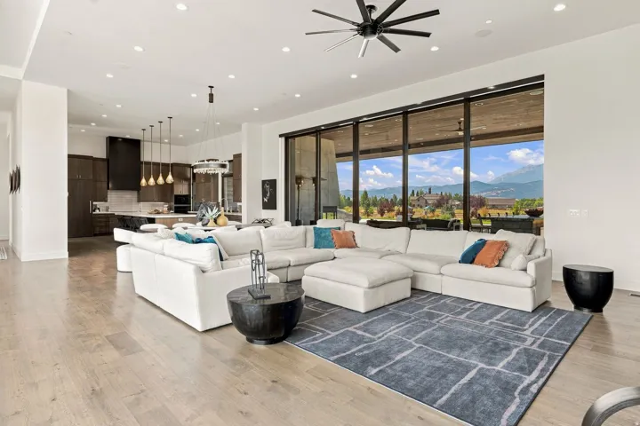 Expansive open-concept living space with wood-finish flooring, a contemporary ceiling fan, recessed lighting, and floor-to-ceiling windows