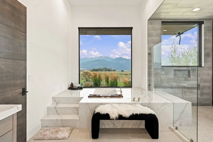 Integrated soaking tub with marble surround, large window with mountain scenery, and glass-enclosed shower with tile walls