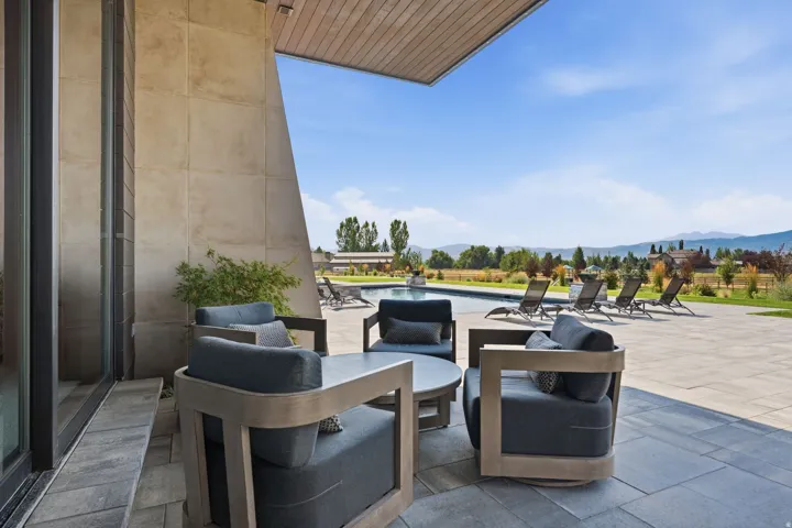 Expansive stone patio with outdoor seating, an inground swimming pool, and a distant mountain backdrop