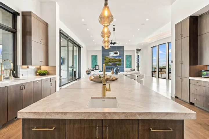 Expansive kitchen island with an undermount sink and brass-finish faucet, custom wood-finish cabinetry, recessed lighting, and large sliding glass doors