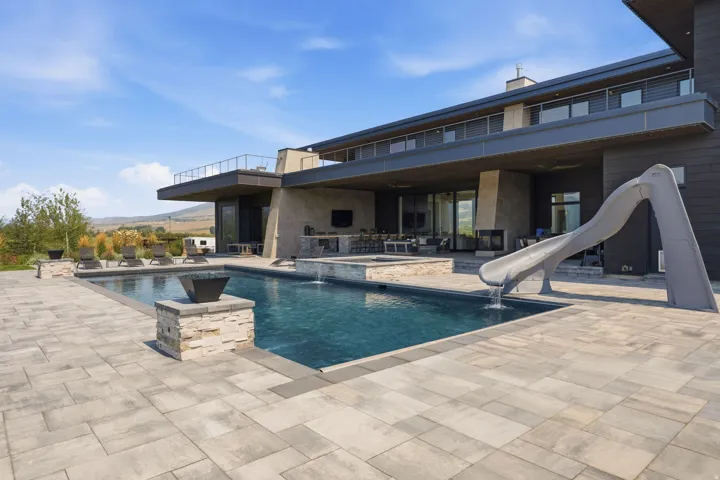 Extensive paver patio with an integrated swimming pool, water slide, and an elevated spa