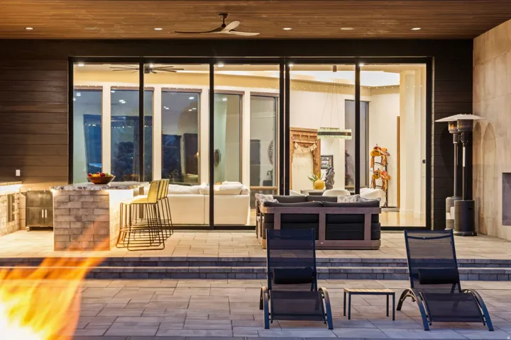 Outdoor living area featuring an integrated kitchen with a stone-clad bar, extensive paver patio, a built-in outdoor fireplace, and large sliding glass doors