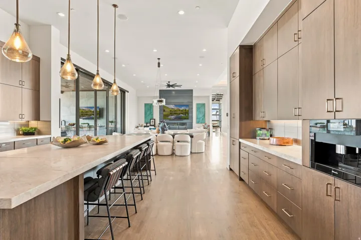 Expansive open-concept kitchen featuring an oversized island, wood-finish cabinetry, built-in appliances, pendant lighting, and wood-finish flooring