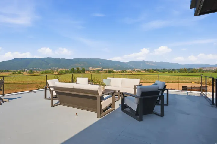 Expansive outdoor patio with glass panel railing overlooking distant mountains and fields