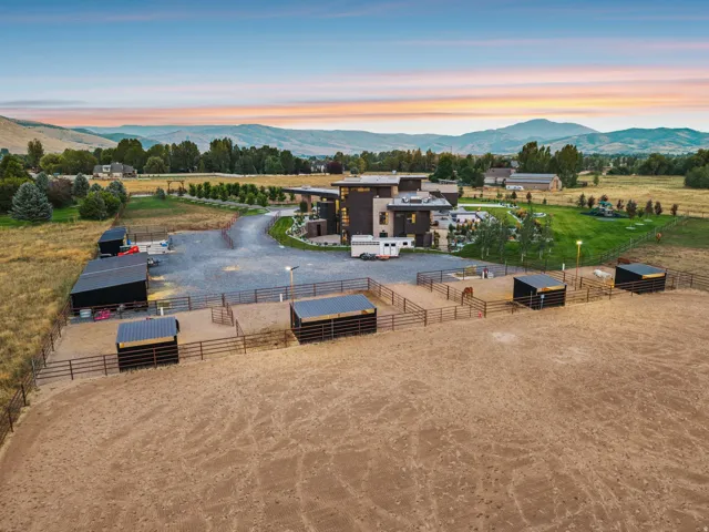 Expansive property featuring a modern architectural residence, multiple fenced animal pens with shelters, a large gravel driveway, a separate barn structure, and a groomed lawn area