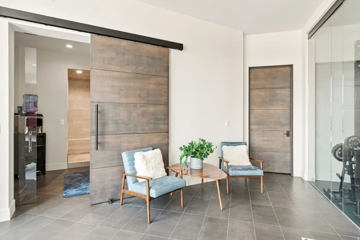 Large format tile flooring, wood-finish interior doors, barn door with black hardware, and floor-to-ceiling glass paneling