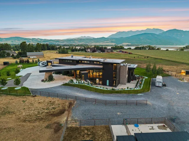 Contemporary residence featuring a flat roofline, extensive window walls, a concrete driveway, and a gravel parking area