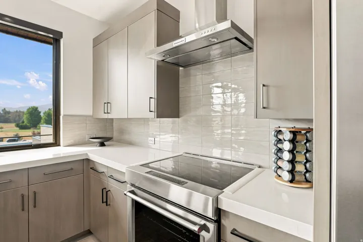 Sleek kitchen featuring light wood-finish cabinetry, a large window, a stainless steel range with a matching hood, and solid surface countertops