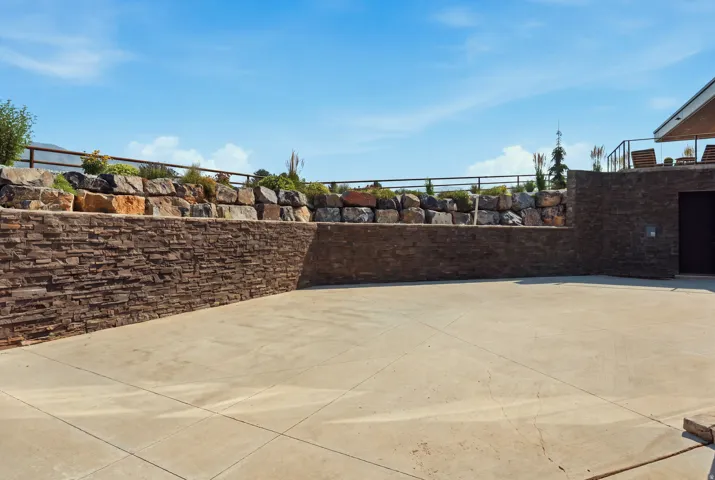 Concrete patio with stacked stone retaining walls and an upper landscaped terrace