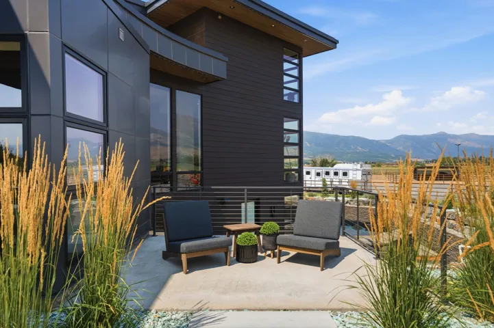 Modern architectural design featuring dark paneling, extensive window placement, and a concrete patio