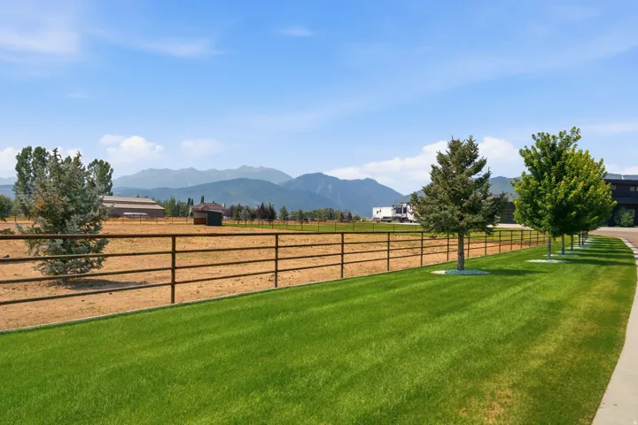 Expansive lawn with mature trees, a multi-rail fence, and mountainous backdrop
