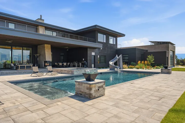 Rectangular swimming pool with integrated spa, expansive paver patio, outdoor fireplace, covered outdoor living area, and modern architectural design