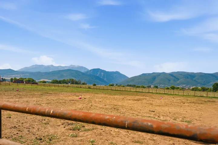 Expansive open field with a wood perimeter fence, surrounded by distant mountains and natural scenery