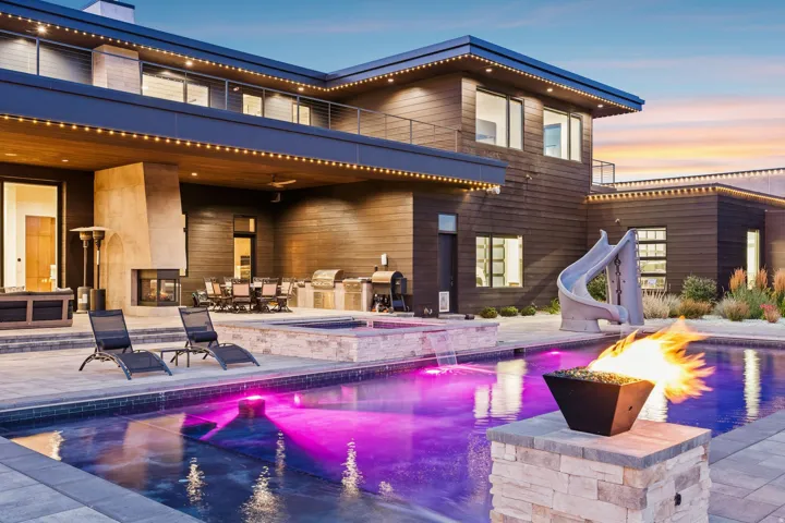 Modern exterior with dark wood siding, a multi-level deck, a built-in outdoor kitchen, a swimming pool with a slide, and a stone fire pit