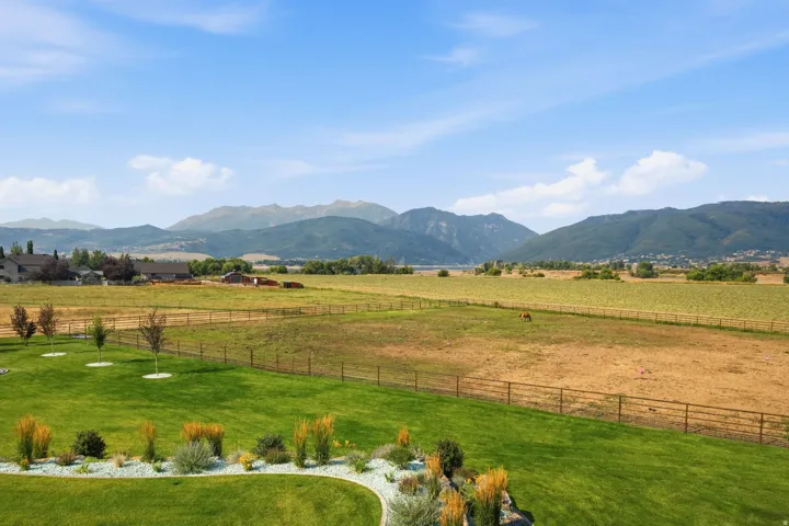 Expansive green lawn with decorative landscaping, fencing, and distant mountain scenery