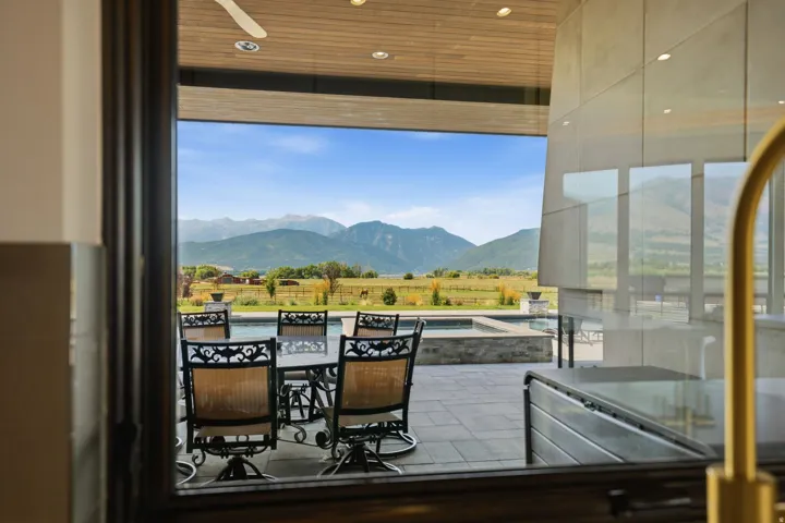Expansive outdoor entertaining space featuring a composite deck with cable railing system, multiple lounge seating areas, and panoramic mountain vistas framed by floor-to-ceiling glass walls