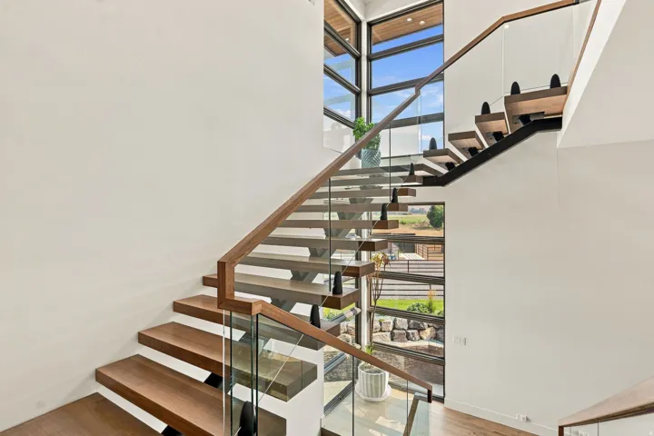 Floating staircase with wood treads, glass panel railing, and a wood handrail
