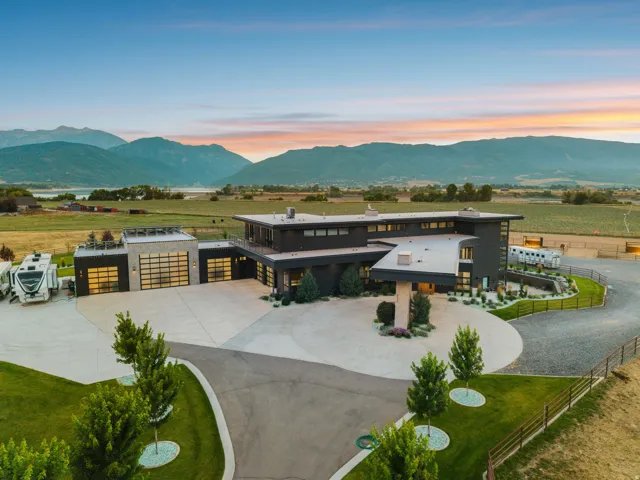 Modern architectural design with a flat roofline, extensive glass garage doors, a circular drive, and lush green landscaping