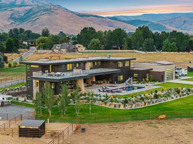 Modern architectural design with multiple outdoor living areas, an integrated swimming pool with slide, manicured lawns, and adjacent fenced pastures