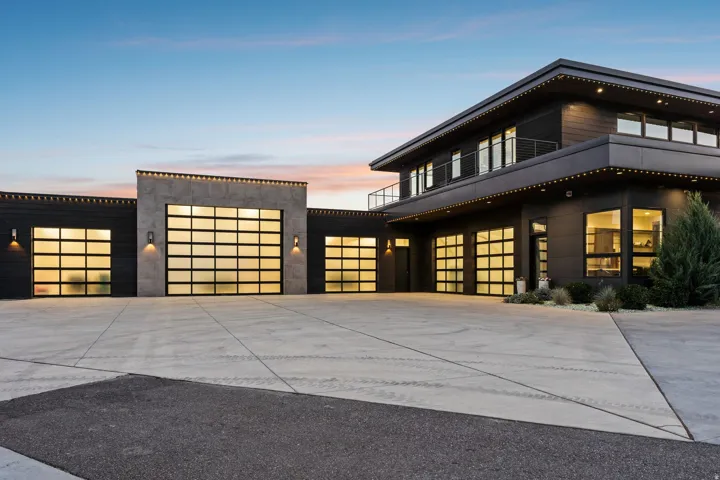 Contemporary exterior with dark siding, extensive glass garage doors, a concrete accent wall, a second-story balcony, and multiple large windows