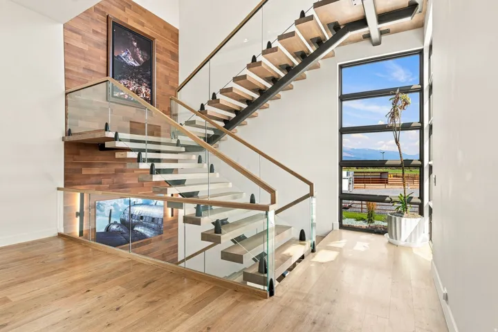 Floating staircase with glass railings, wood-finish treads, and a wood accent wall
