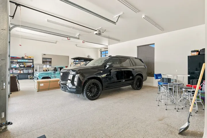 Attached garage with a textured concrete floor, multiple fluorescent light fixtures, and a roll-up garage door