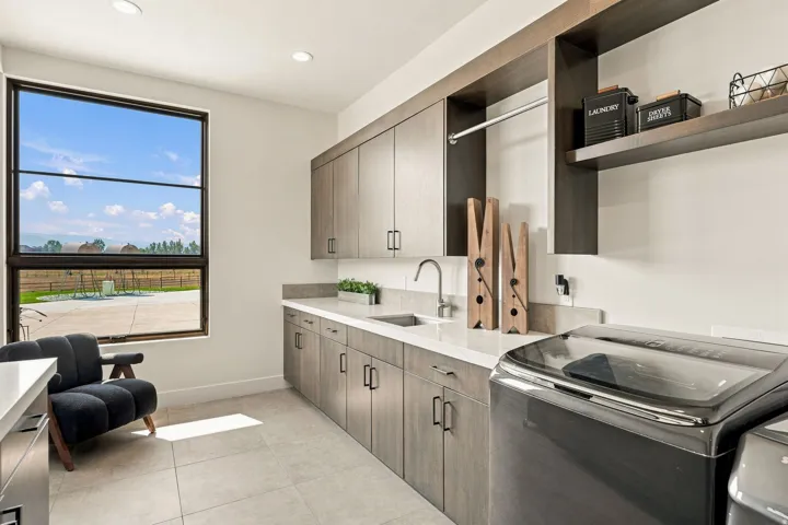Spacious utility room featuring a large window, extensive wood-finish cabinetry, light-toned countertops, integrated sink, and built-in shelving with a hanging rod