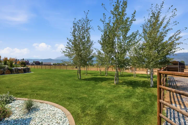 Expansive grassy areas, mature trees, a decorative rock garden, and a rustic wood fence