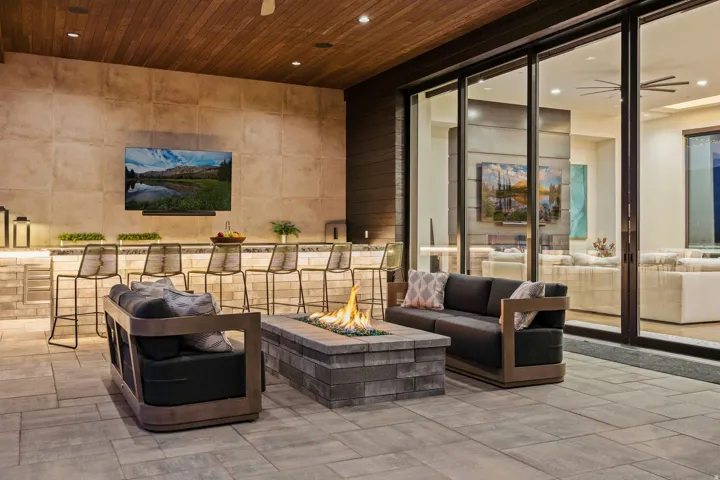 Covered outdoor patio with a wood-plank ceiling, stone-clad walls, a built-in bar with under-cabinet lighting, a fire pit, and large sliding glass doors