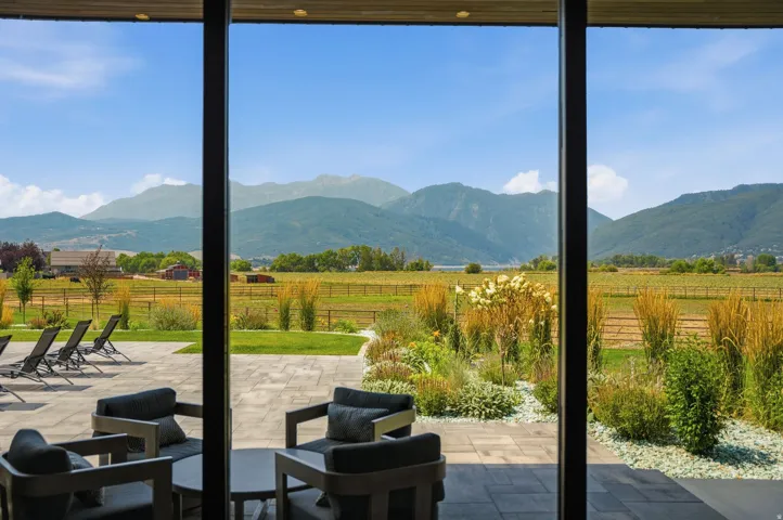 Expansive outdoor patio with large format pavers, an integrated garden bed with decorative white stone, and full-height windows framing mountain and field scenery