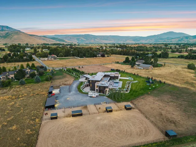 Expansive property featuring a contemporary residence, multiple outbuildings, fenced equestrian areas, a manicured lawn, and mature trees