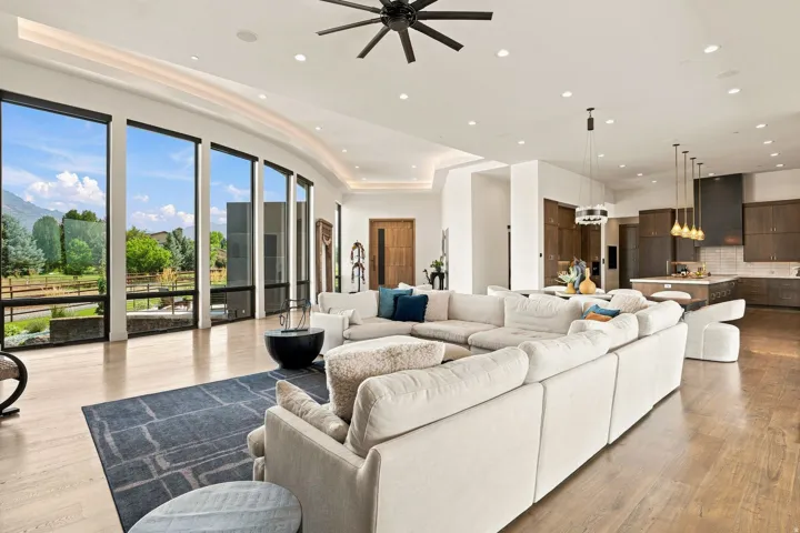 Expansive living space featuring full-height windows, light wood-finish flooring, recessed lighting, and a modern ceiling fan