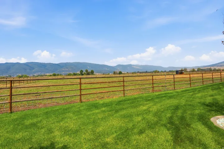 Expansive green lawn bordering a metal fence, with a distant mountain range and clear blue sky