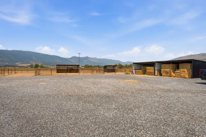 Gravel lot with multiple covered stalls, fenced corrals, and mountain backdrop