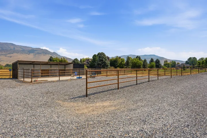 Expansive gravel area with metal fencing, open-sided shelter, and mountain backdrop