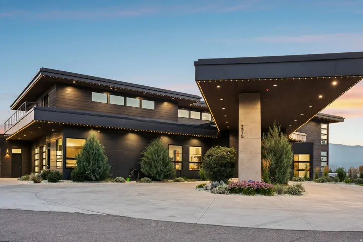 Contemporary exterior featuring a cantilevered entry canopy, expansive windows, multiple upper-level balconies with glass railings, and a concrete paver driveway