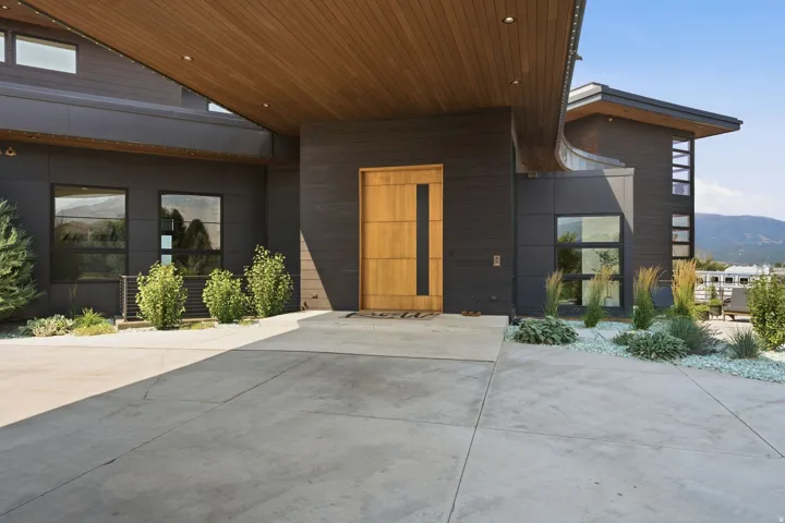 Contemporary exterior featuring dark siding, a wood-finish soffit, a light wood-finish front door, a concrete driveway, and minimalist landscaping