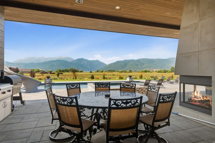 Expansive patio with an outdoor kitchen, built-in fireplace, and a swimming pool, all set against a mountainous backdrop