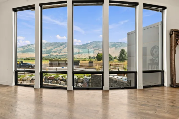 Expansive multi-panel glass doors with black aluminum framing open onto a scenic landscape vista featuring rolling hills and distant mountains
